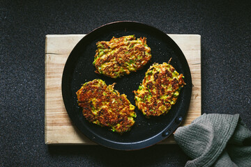 Vegetable zucchini and carrot fritters on a frying pan and a wooden cutting board, top view