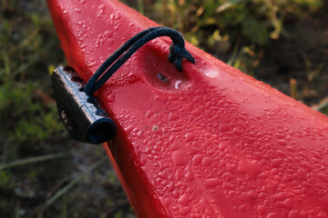 Drops of water and a spider on the bow of a red plastic kayak. Black handle for carrying the boat. 