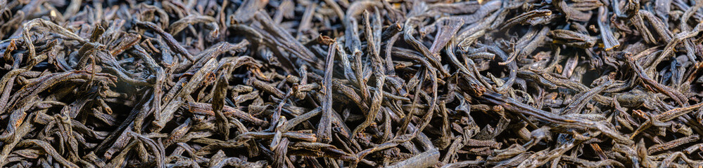 Fototapeta premium Scattered black tea close-up. panoramic view of dry tea leaves. Macro shot of tea brewing.