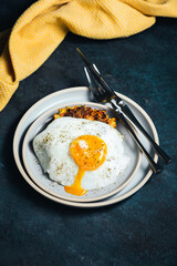 Vegetable zucchini and carrot fritters and an egg with a runny yolk on top, served on a blue plate, knife and fork, yellow towel, dark backdrop