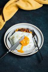 Vegetable zucchini and carrot fritters and an egg with a runny yolk on top, served on a blue plate, knife and fork, yellow towel, dark backdrop