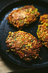 Vegetable zucchini and carrot fritters on a frying pan and a wooden cutting board, close-up photo