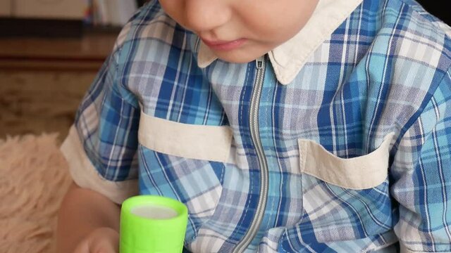A little boy turns on and off a flashlight looking at it close-up