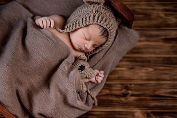 Newborn baby, beautiful infant lies and holding a tiny teddy bear in the bed on wooden background, Copy space