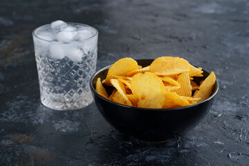 a cup of chips, a clear glass of soda with ice on a dark background, fluted chips