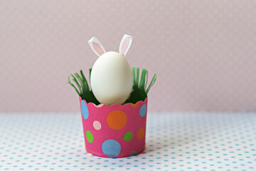 White chicken egg with bunny ears in an eco-friendly pink paper tray, box. Happy Easter holiday concept.