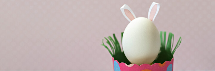 White chicken egg with bunny ears in an eco-friendly pink paper tray, box. Happy Easter holiday concept. English text Happy Easter .Banner