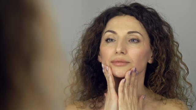 Beautiful middle-aged woman massages her face and neck with light movements. Daily skin care.