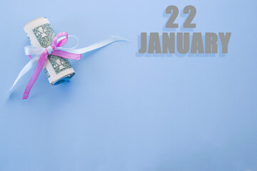 calendar date on blue background with rolled up dollar bills pinned by blue and pink ribbon with copy space. January 22 is the twenty-second day of the month