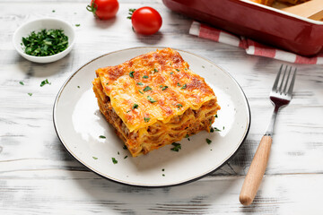 Portion of  ground beef lasagne topped with melted cheese and garnished with fresh parsley served on a gray plate .