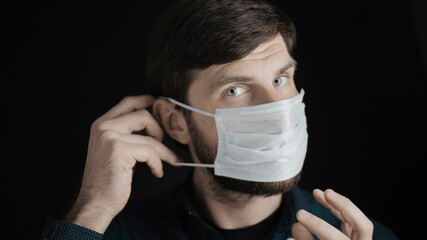 Attractive bearded man is putting on surgical mask on his face for corona virus covid-19 prevention. Infection protection, quarantine and epidemic concept. Slow motion close up front view 4k video.