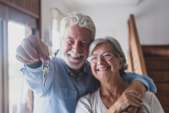 Happy senior old aged woman and man customer landlord hold key to new house apartment give to camera, older retired couple of seniors hand real estate owner make sale purchase property deal concept