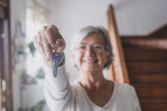 Happy senior old aged woman customer landlord hold key to new house apartment give to camera, older retired female hand real estate owner make sale purchase property deal concept, close up view.