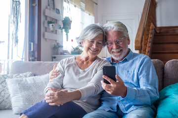 Couple of two old and mature people at home using tablet together in sofa. Senior use laptop having fun and enjoying looking at it. Leisure and free time concept.