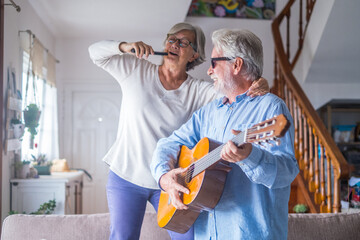 Couple of two happy seniors or mature and old people singing and dancing together at home indoor....