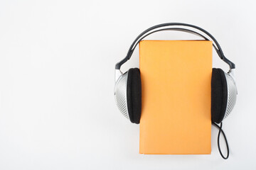 Audiobook on white background. Headphones put over yellow hardback book, empty cover, copy space for ad text. Distance education, e-learning concept. Top view