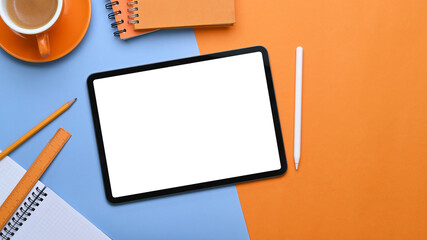 Empty screen of digital tablet on two tone background with office supplies.