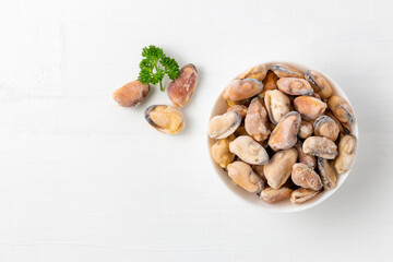 Frozen mussels with parsley on white wood with copy space. Healthy and nourishing diet concept. Uncooked seafood on table.