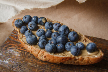 Healthy sandwich. Toast with peanut butter and blueberries on a wooden kitchen board on a wooden table, closeup. Healthy breakfast.