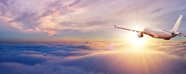 Passenger jetplane flying above clouds in sunset - obrazy, fototapety, plakaty
