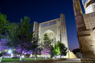 Fototapeta na wymiar night view of huge madrasah with violet backlight with trees in inner yard 