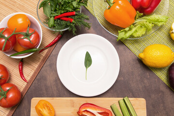 Different vegetables for cooking and one spinach green leaf on empty white plate. Diet, fasting, vegan, vegetarian, healthy food concept