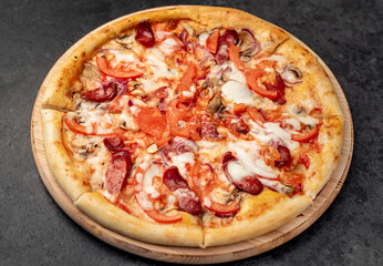 pizza with sausages, mushrooms, tomatoes and cheese on a stone background