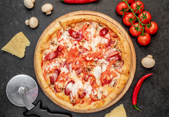 pizza with sausages, mushrooms, tomatoes and cheese on a stone background