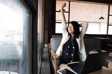 Smiling Asian businesswoman is stretch lazily at workplace in modern office or relaxing at coffee shop. Lifstyle of people with techonology concept.