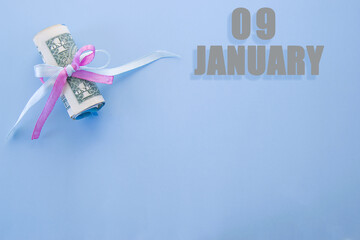 calendar date on blue background with rolled up dollar bills pinned by blue and pink ribbon with copy space. January 9 is the ninth day of the month