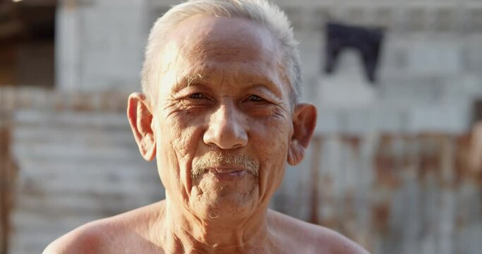 Slow motion scene of white-haired Asian elderly men do not wear clothes because of hot weather, poor status, older than seventy is laughing happily on the sunset light in the evening.