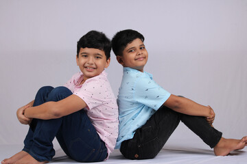 Indian siblings sitting together on white background.