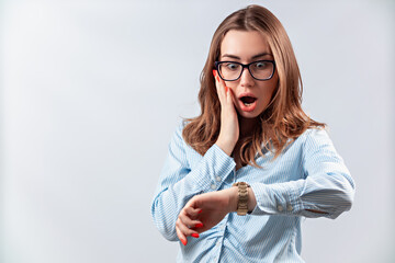 beautiful girl in a blue shirt and glasses looks at the clock on a white background. isolated