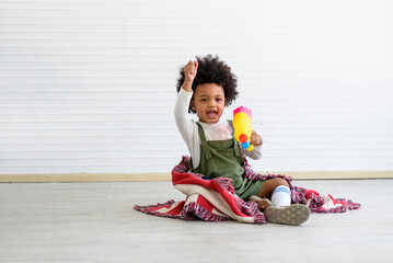  kids with toys sitting on the floor looking straight at the camera. Look cute.