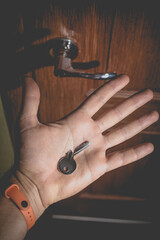 A man holds in his hand a small light broken key against the background of a door lock.