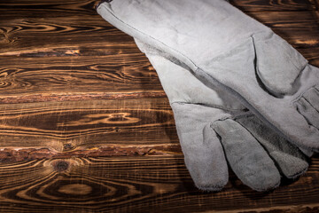 White leather welder gloves on a wooden background. A studio photo with hard lighting.