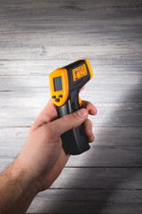 A man holds a yellow-black pyrometer on a wooden background. A device for non-contact temperature measurement.