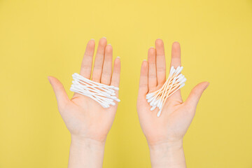 Hands hold plastic cotton swabs and bamboo cotton swabs. Hygiene items on a green background. The concept of zero waste