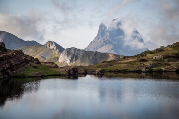Stunning view of a beautiful mountain surrounded by clouds in the Pyrenees with a quiet lake in the foreground