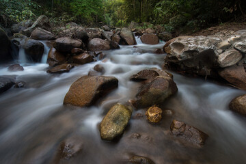 Naklejka na ściany i meble Waterfall landscape. Beautiful hidden waterfall in tropical rainforest. Foreground with big stones. Slow shutter speed, motion photography. Travel and adventure.