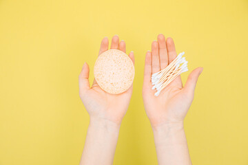 Hands hold  bamboo cotton swabs and biodegradable sponge with cotton and linen. Hygiene items on a yellow background. The concept of zero waste