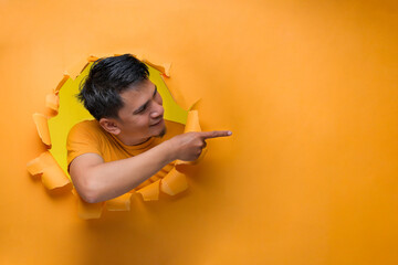 Asian man with happy expression pointing a copy space to advertise something, on torn paper hole