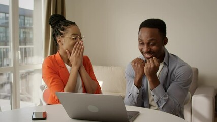 Charming african american couple recieved unbelievable good news and are extremely happy about it. Both giving high fives in front of a laptop