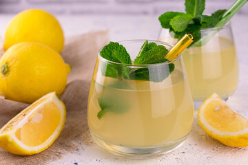 
Two glasses of freshly squeezed lemon juice with a mint branch on a white background.