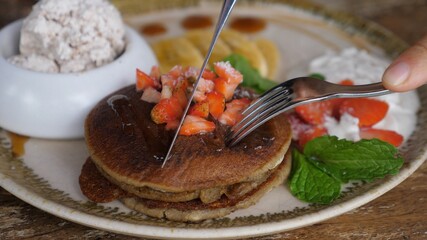 Hands cutting stack of pancakes with fork and knife. Healthy plant based breakfast 