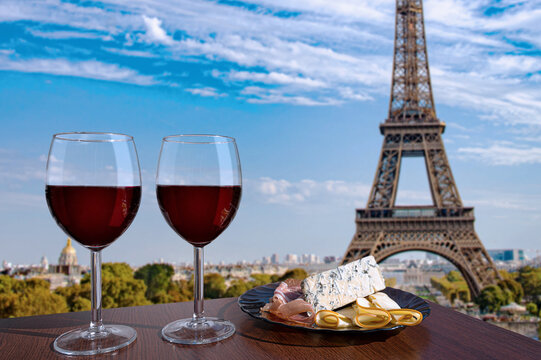 Two glasses of red wine with snacks with view of Paris and Eiffel tower. Glass of red wine with different snacks - plate with ham, sliced, blue cheese. Couple, romantic celebration. Cafe with view.