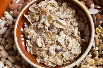 Overhead view of a pile of toasted rice, whole wheat, and barley flakes with chocolate shavings with different dry nuts on the background. Food, mixed dry fruits, and cereals.