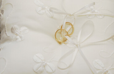 Dos anillos de oro unidos a un pequeño cojín blanco con flores bordadas. Vista cercana de las joyas para el día de la boda.