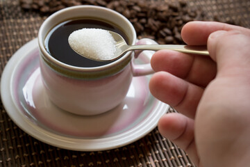 Hand adding sugar with spoon over a cup of coffee