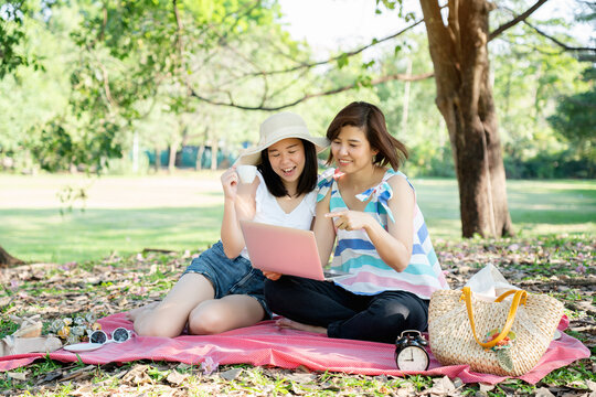 Asian family Two women picnic in park during summer vacation. Happy two sister sitting on using laptop for shopping online. Traveler lesbian couples relax during holidays. Concept Health insurance